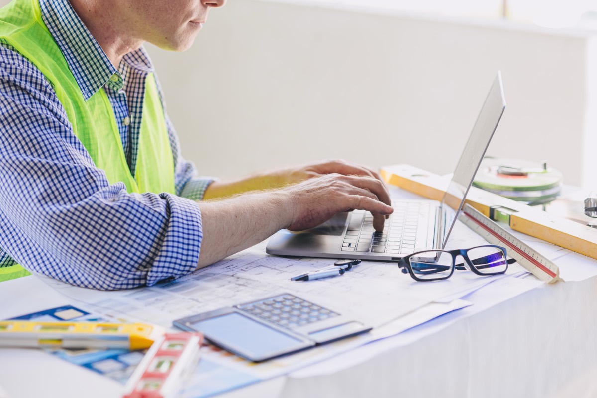 A contractor typing an estimate over a set of printed plans